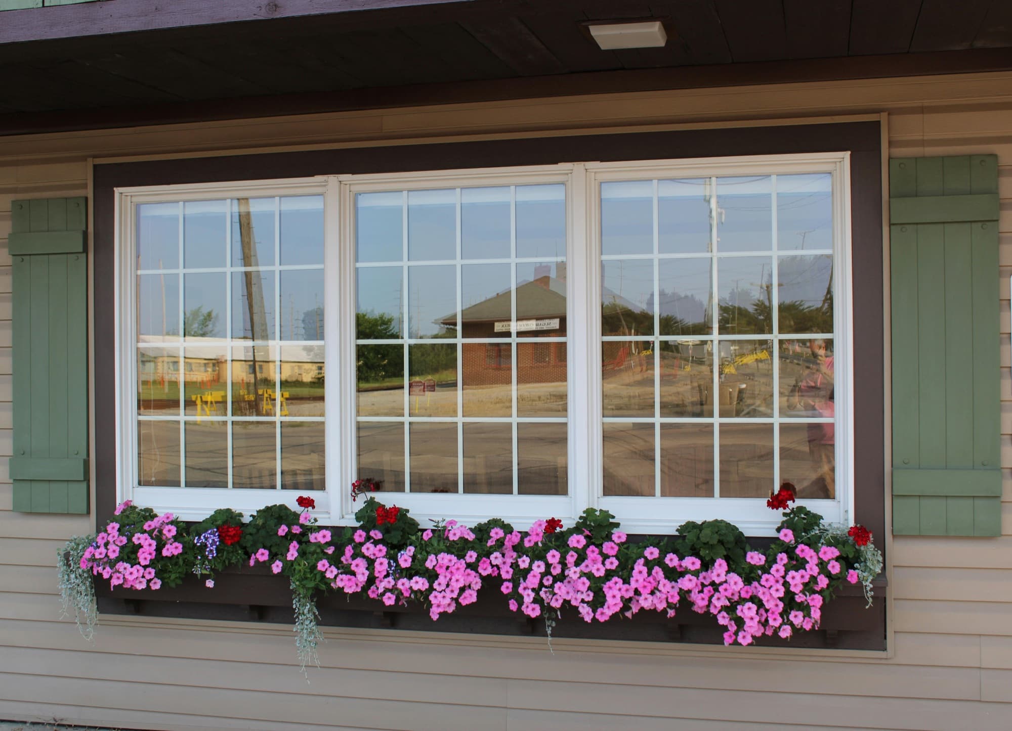 Triple residential windows with white trim, green shutters, and a pink flower window box on a sided home